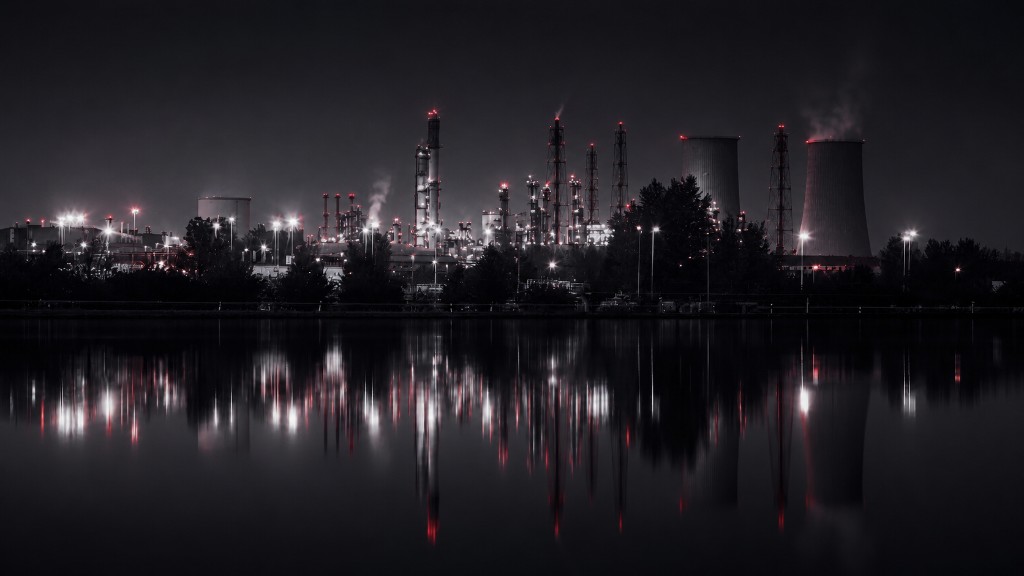 Oil and gas refinery at night, with illuminated towers, red warning lights, and cooling stacks reflected in calm water.